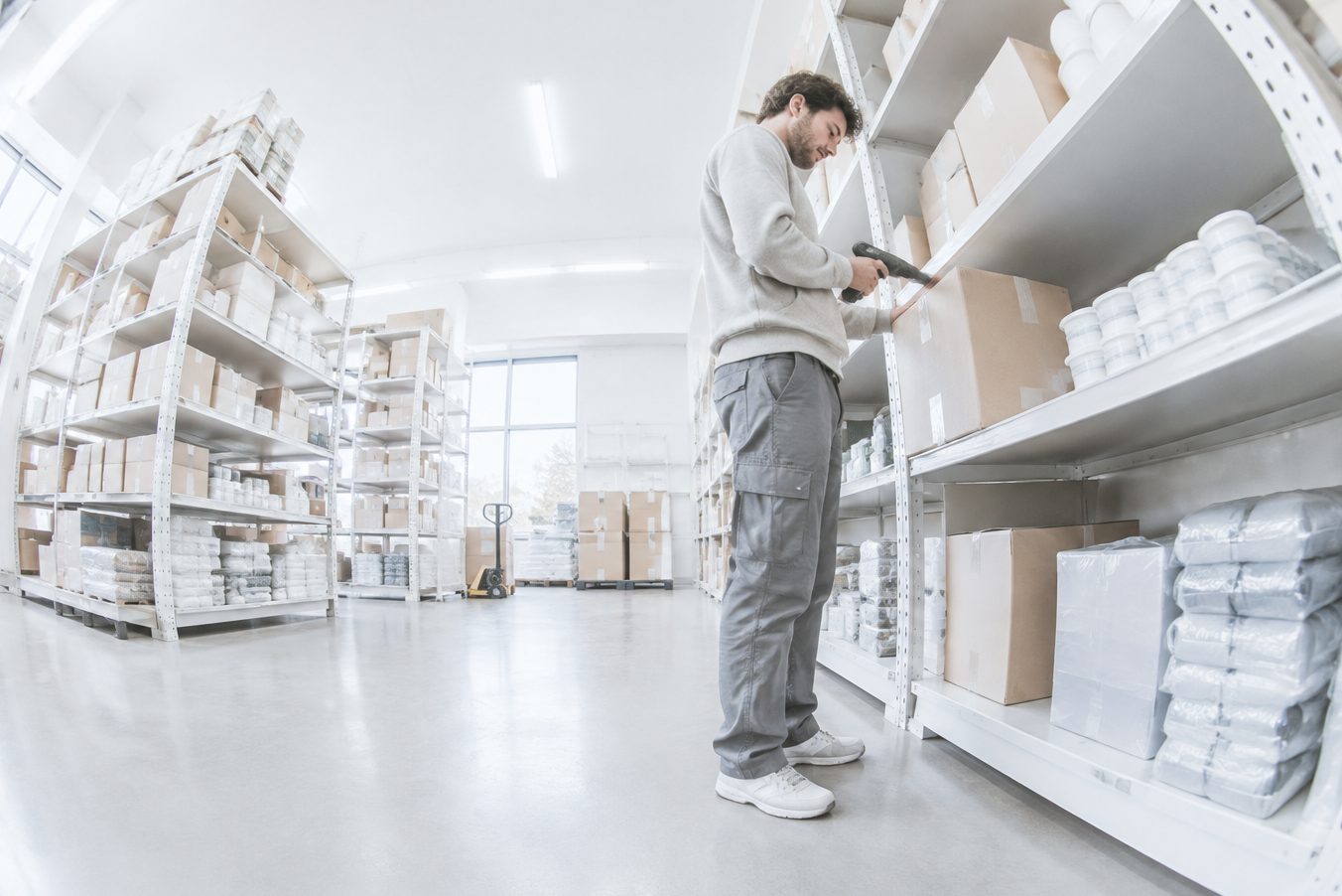 A worker scans a box between the warehouse shelves at a distributor