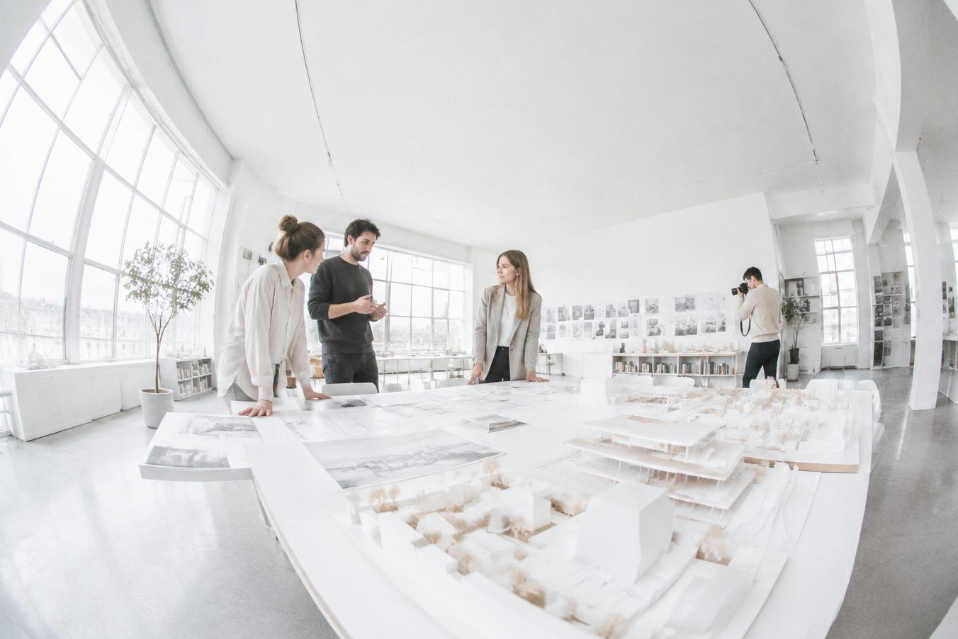 An architecture team gathered around a model while a photographer takes pictures
