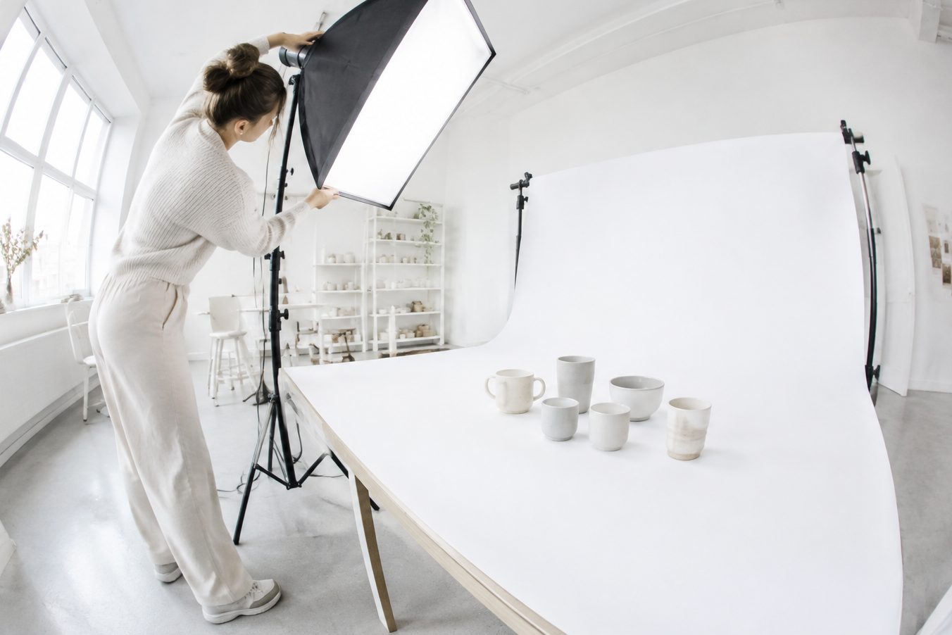 A photographer adjusts the light on ceramic mugs in a studio