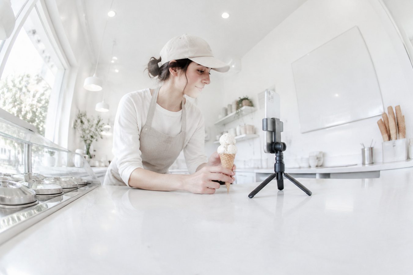 A worker records an ice cream cone with her phone at an ice cream shop